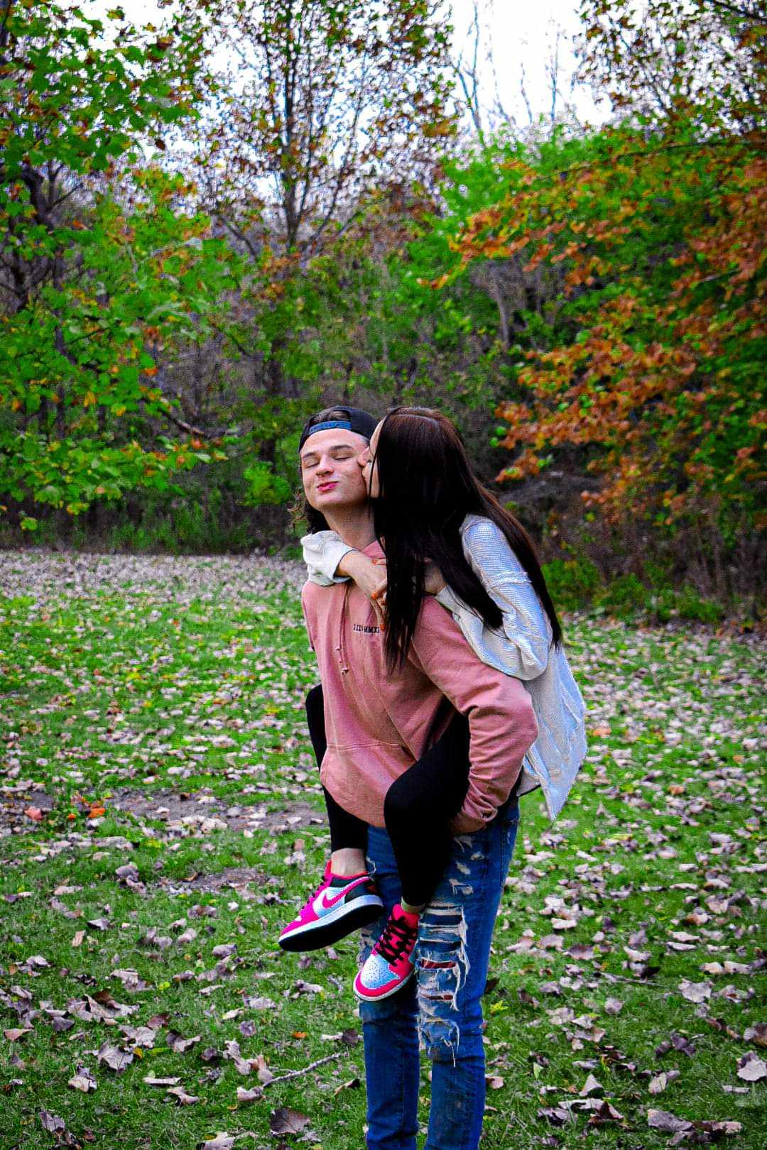 Young couple in autumn park, woman giving piggyback kiss on cheek to man, sweet and affectionate moment