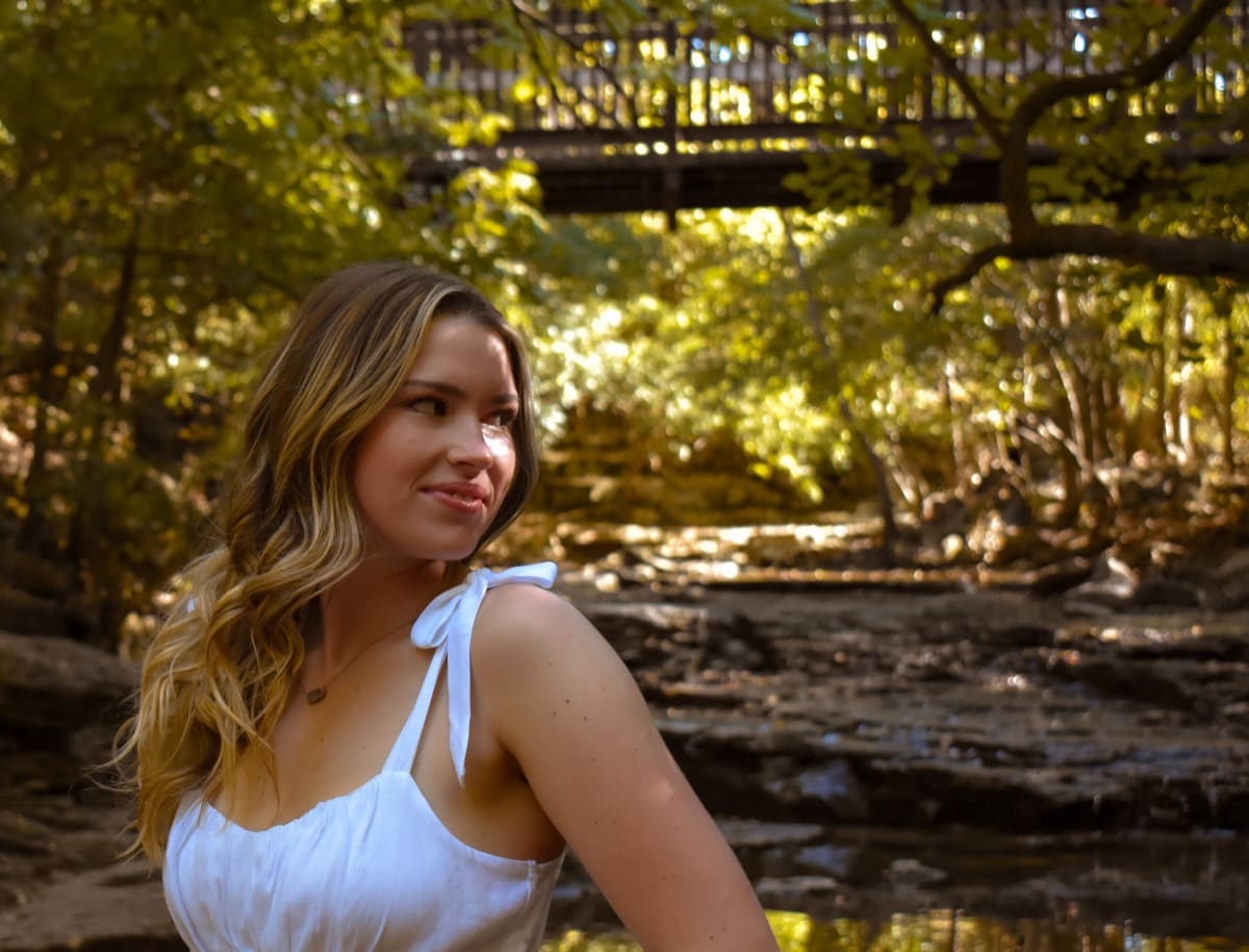 Senior girl sitting beside a creek in the woods in soft natural light