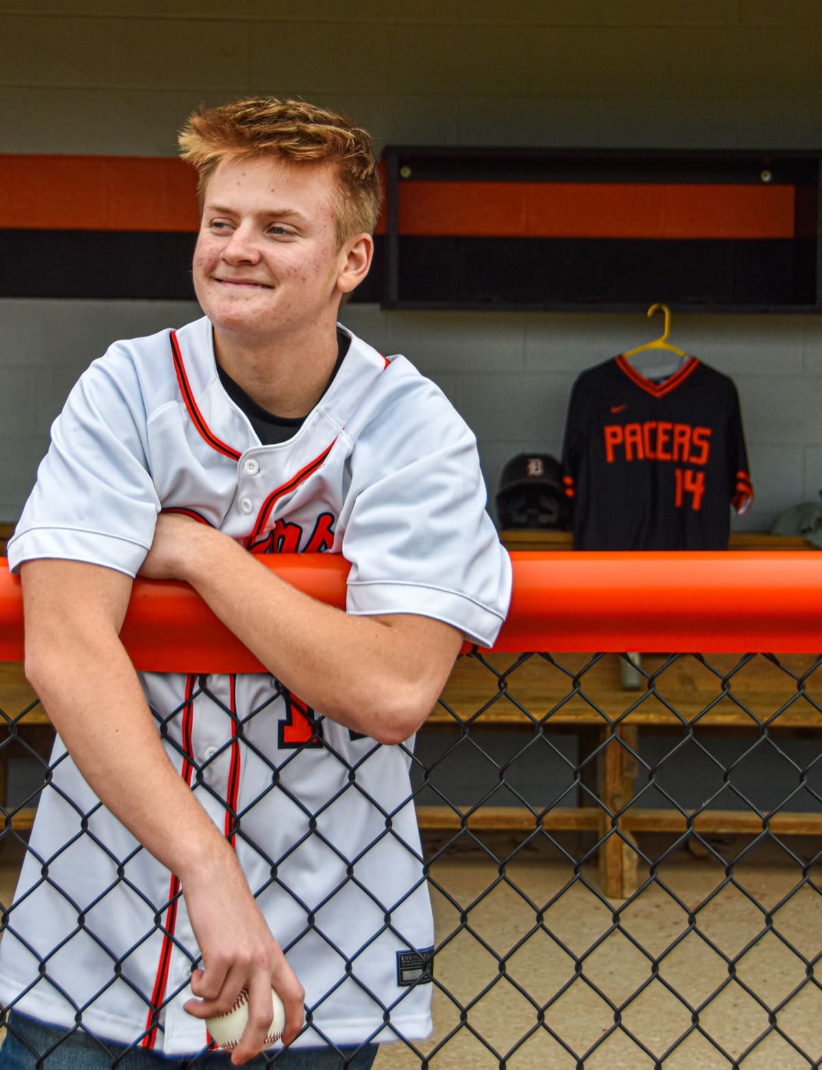 Senior baseball player in his jersey leaning on the dugout rail