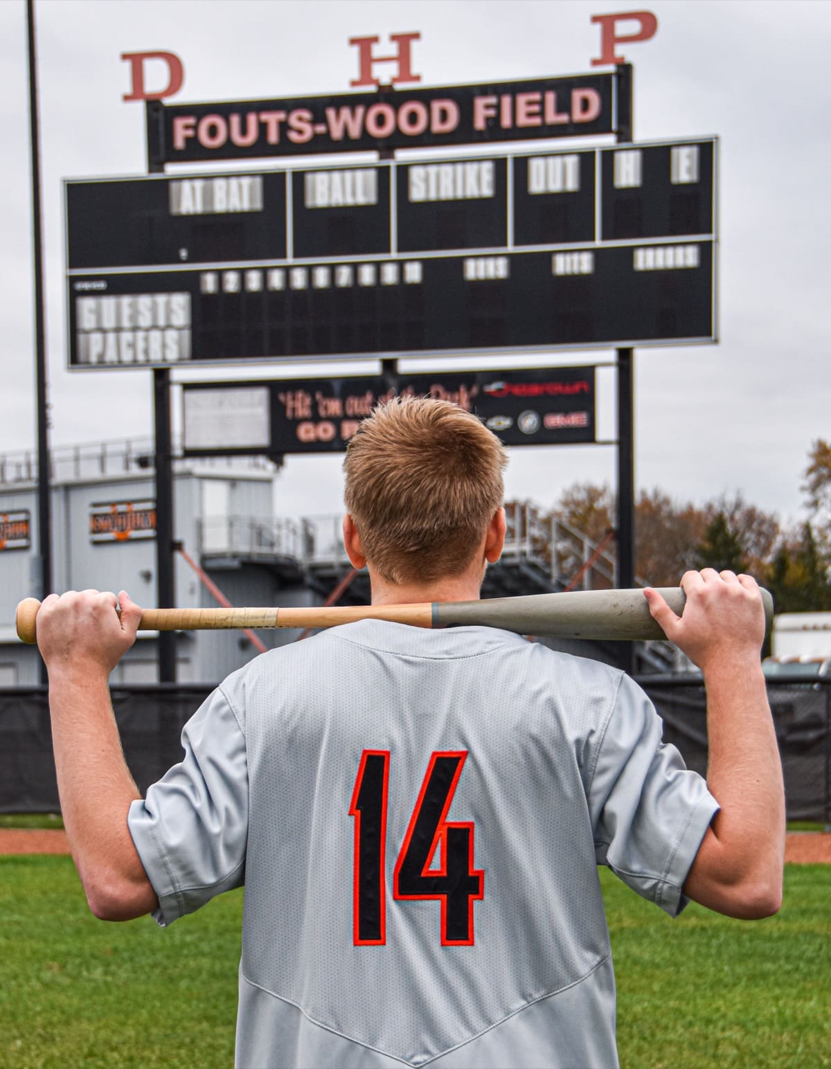 Baseball player number 14 resting a bat on his shoulders under the Fouts-Wood Field scoreboard