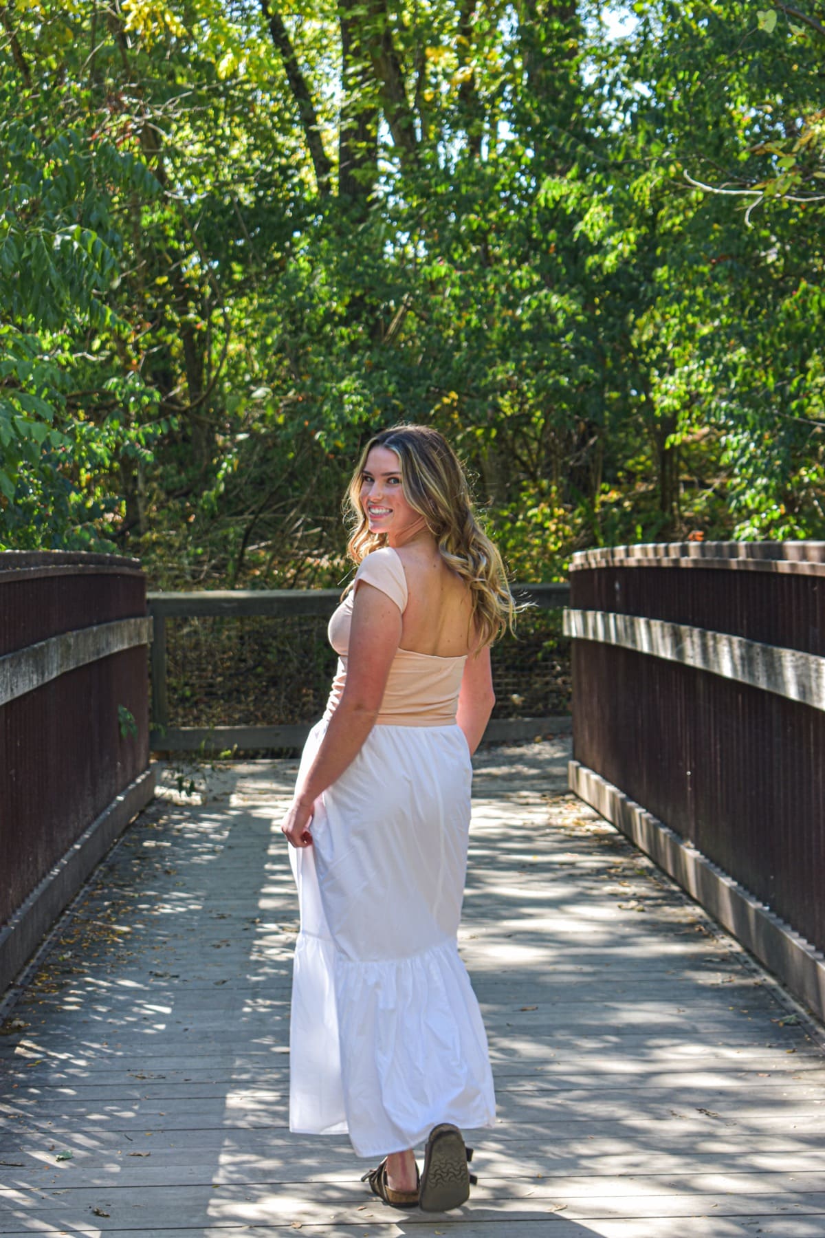 Senior girl in a white dress on a wooden footbridge in the woods