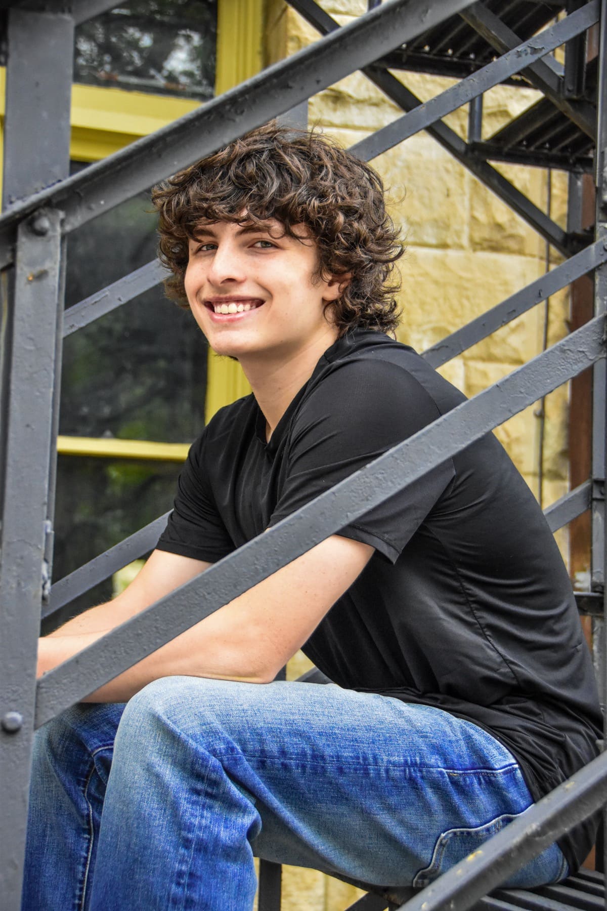 Senior with curly hair sitting on a metal staircase, smiling