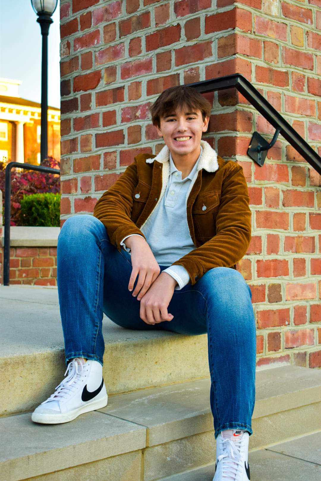 Young man smiling broadly at camera on stone steps with warm golden hour lighting, cheerful and approachable
