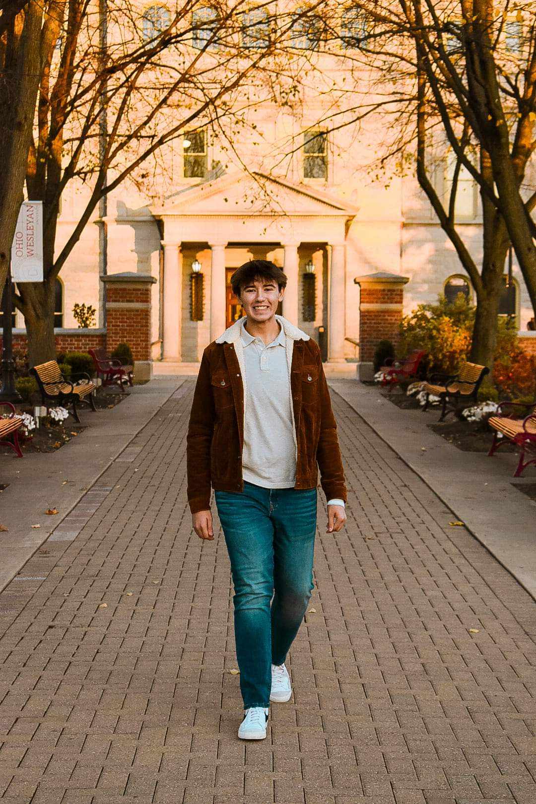 Young man walking on brick campus walkway at Ohio Wesleyan University with classical building and golden sunset light