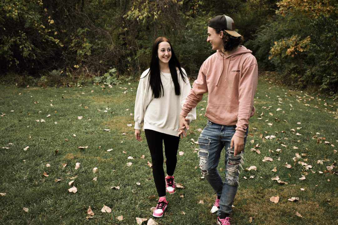 Young couple walking hand-in-hand on leaf-scattered grass in autumn, close-up shot with fall foliage