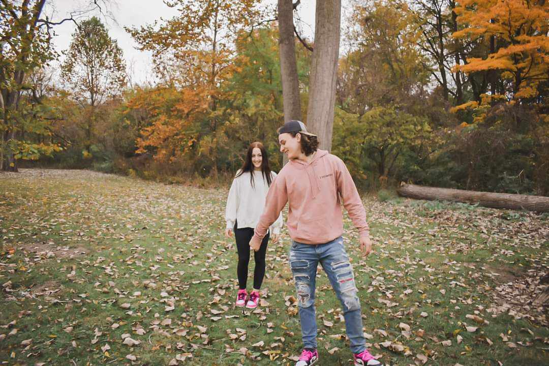 Young couple walking hand-in-hand across autumn field with vibrant fall foliage in background, wide shot