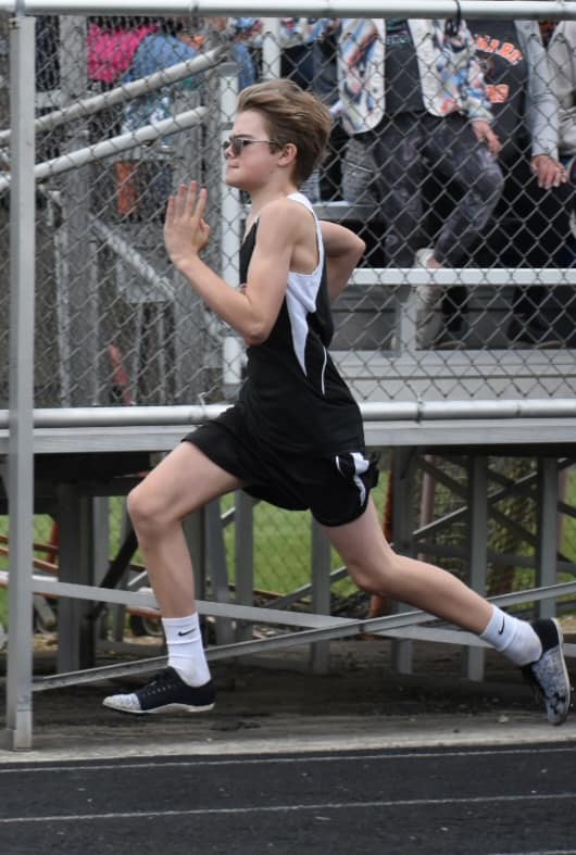 Young track athlete sprinting at full speed with proper form wearing black and white singlet