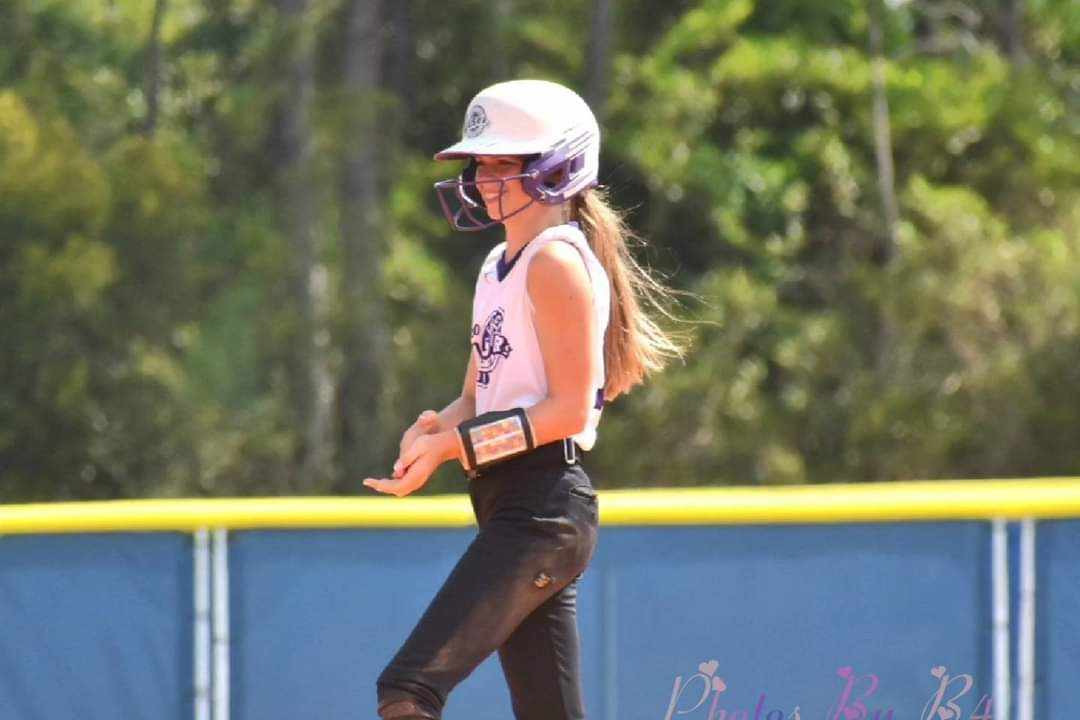 Young softball baserunner in white helmet and navy uniform with dirt-stained pants standing on base path