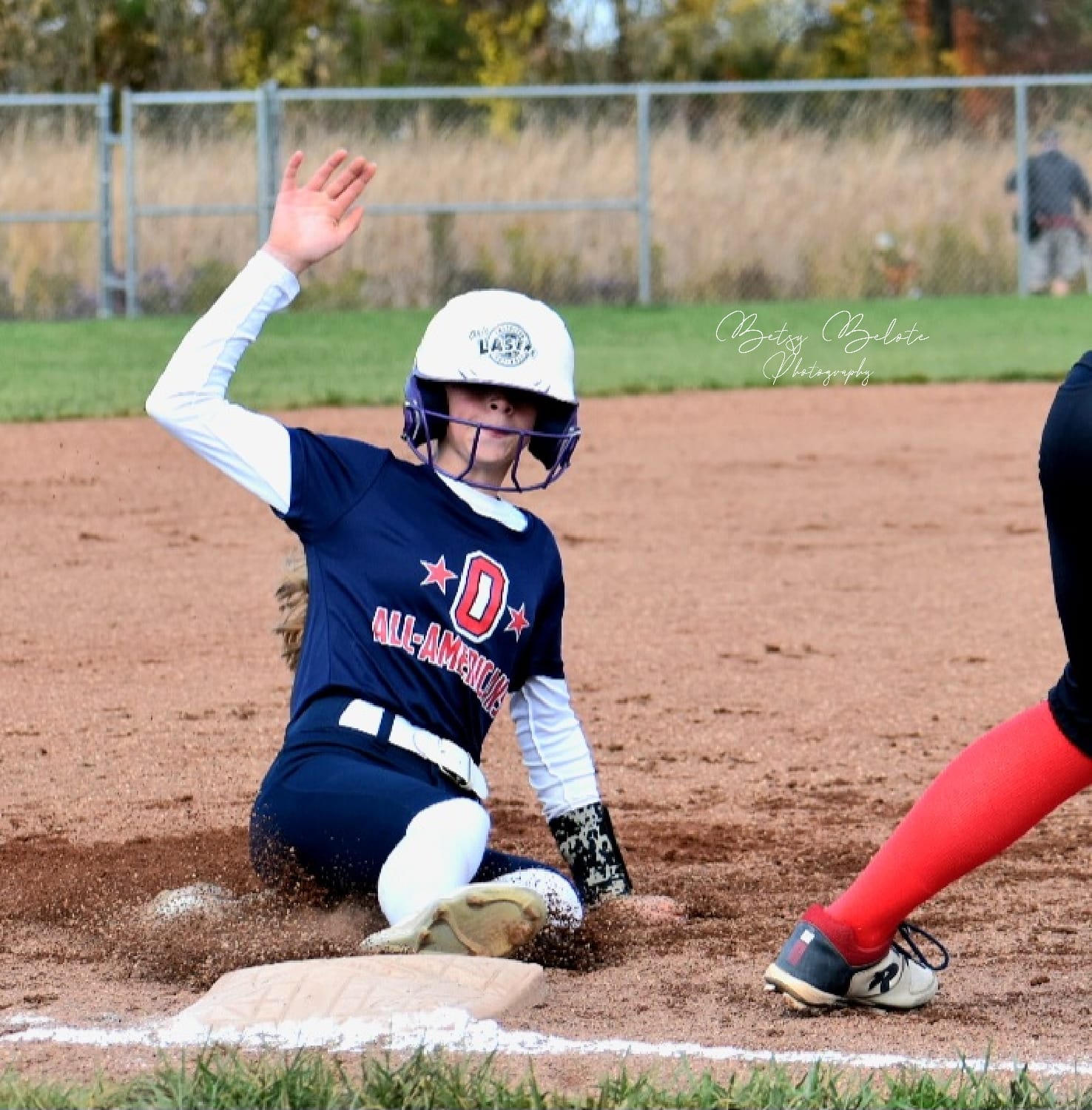 Youth softball player sliding feet-first into base with hand raised high as dirt kicks up around her