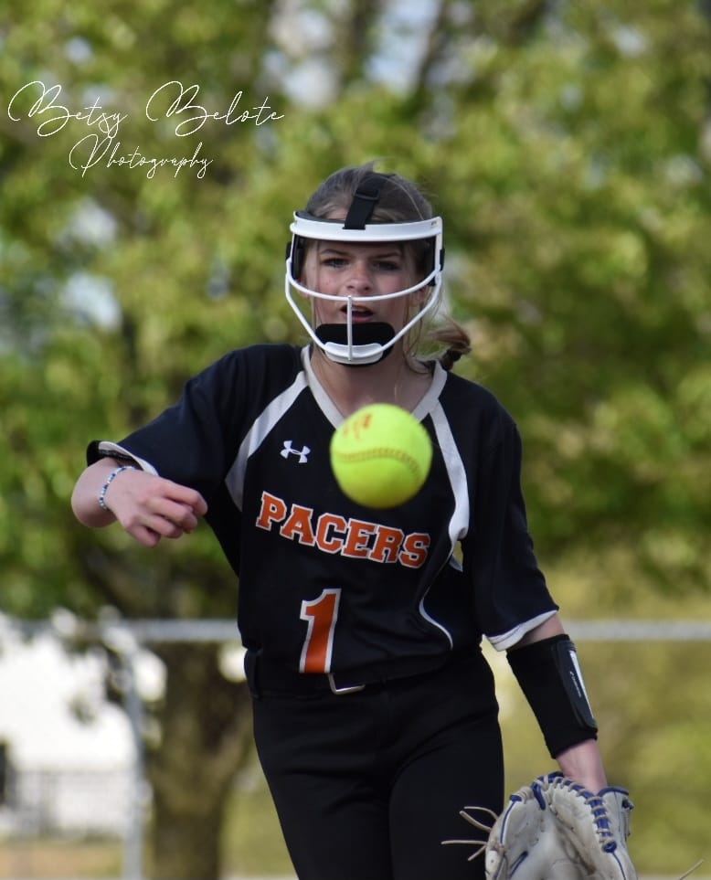 Female softball player in black Pacers jersey fielding yellow softball mid-air during game