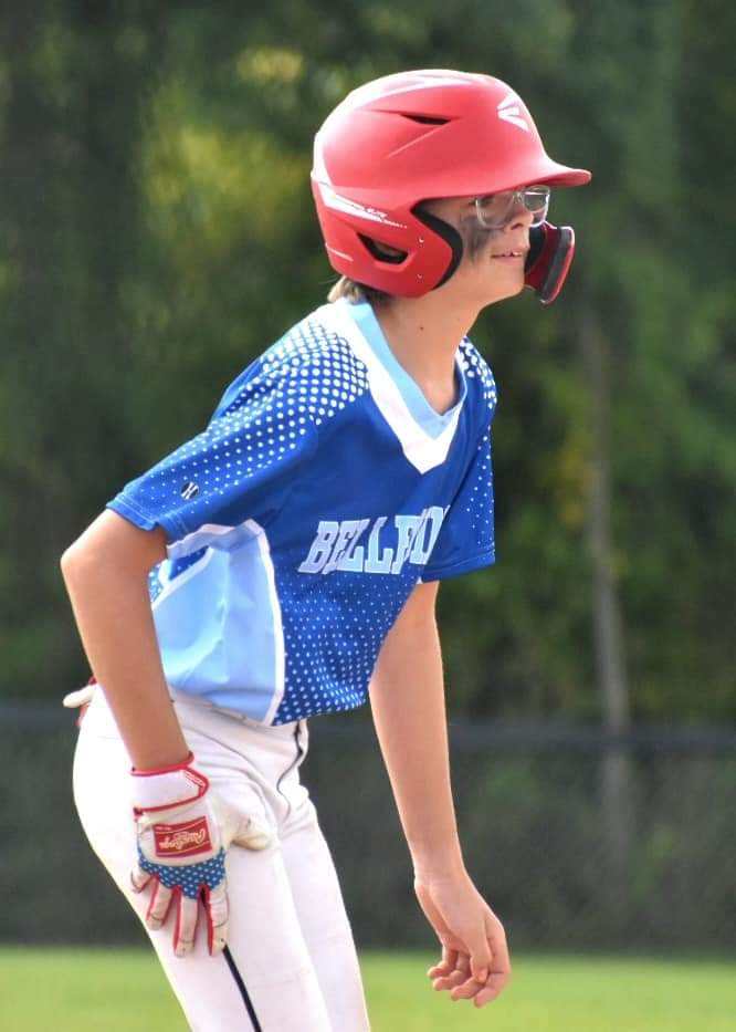 Young male baseball player standing on base in blue Bellepoint jersey with batting gloves tucked in waistband