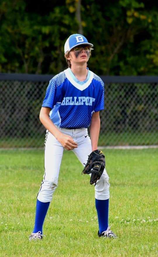 Young male baseball player in fielding position looking upward with black glove on grass field